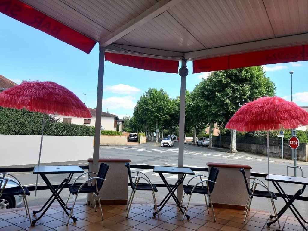 Terrasse ombragée du bar Le Bruit des Glaçons à Albi, tables et parasols roses.